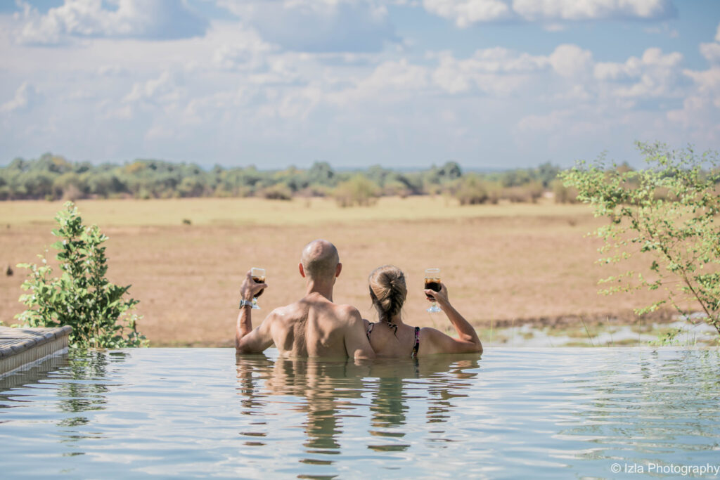 The safari swimming pool at Kafunta River Lodge in South Luangwa - two guests enjoying a glass of wine in the pool and looking out into the plains ahead